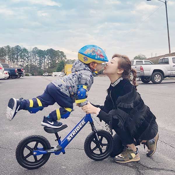Child kissing mom while standing on Strider bike