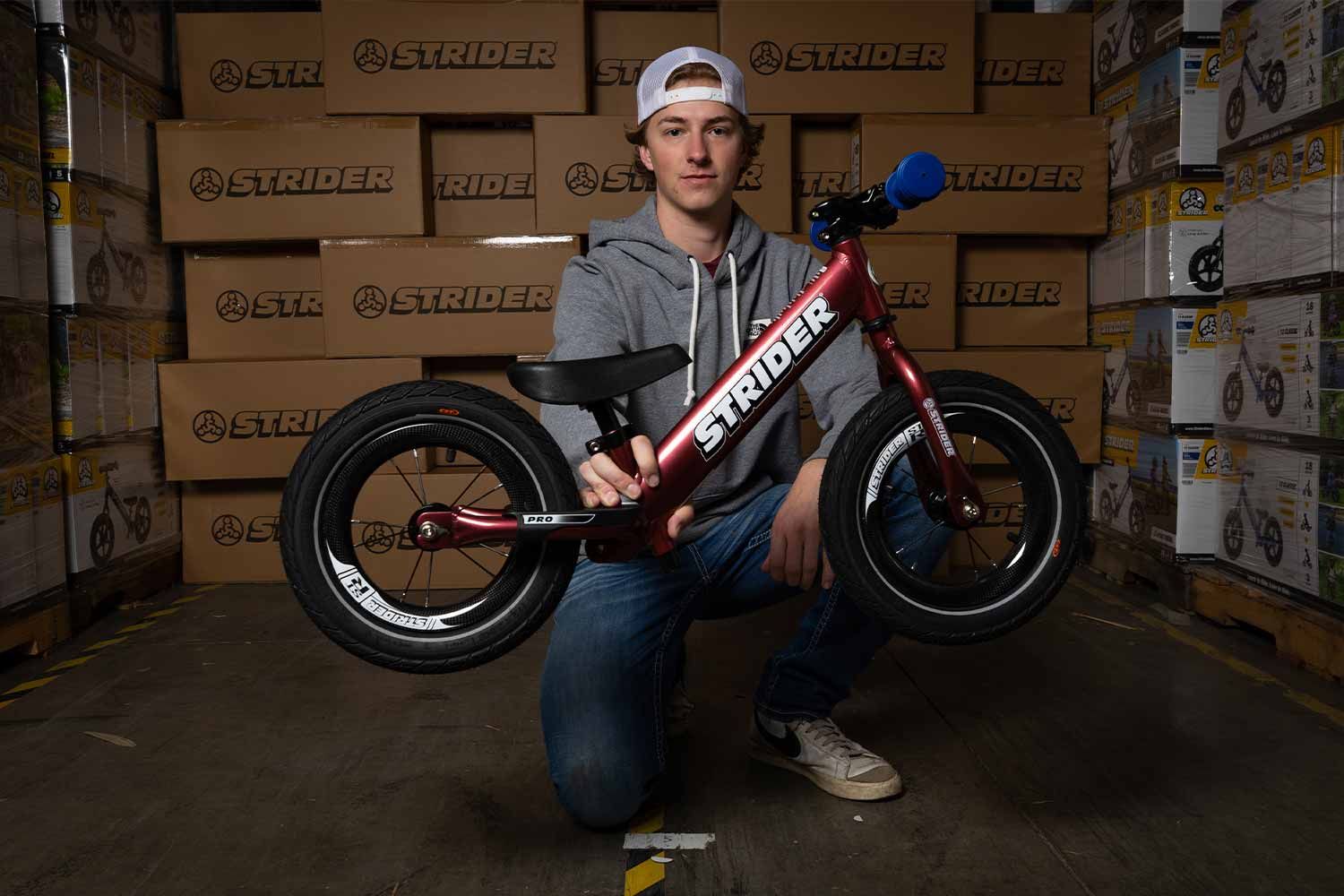Bode McFarland poses with Strider Rider 1 - Race Edition balance bike in the Strider warehouse
