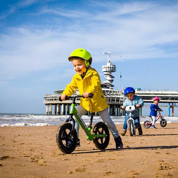 Riding Strider bikes on the beach with a shipping pier in the background