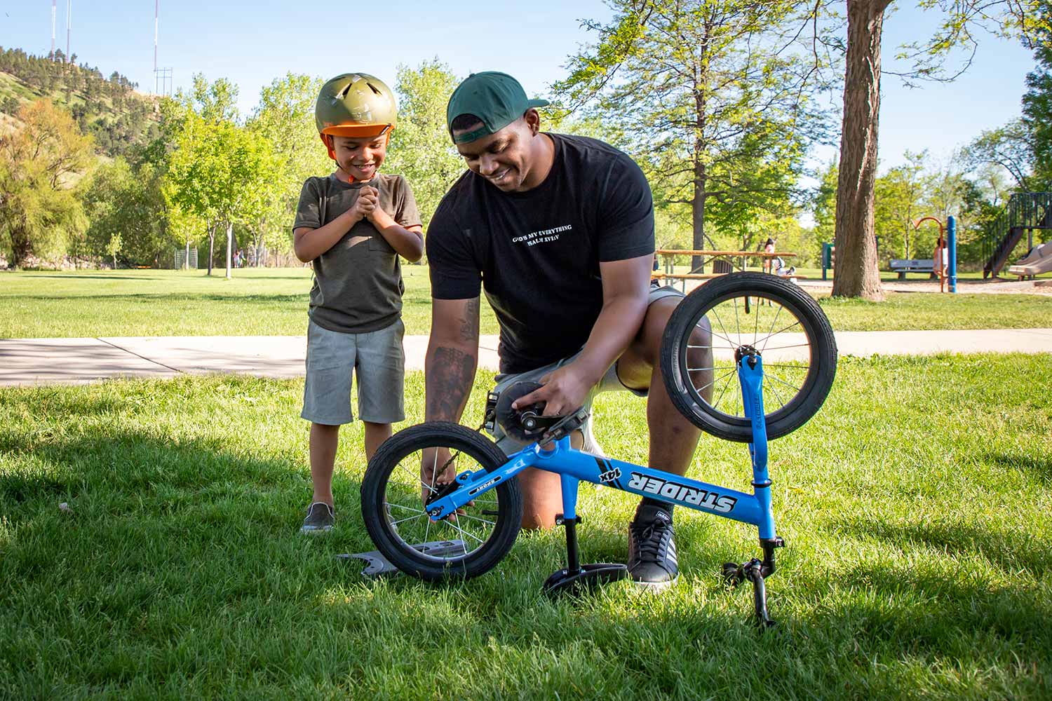 Dad installing Easy-Ride Pedal Kit as child looks on in a park
