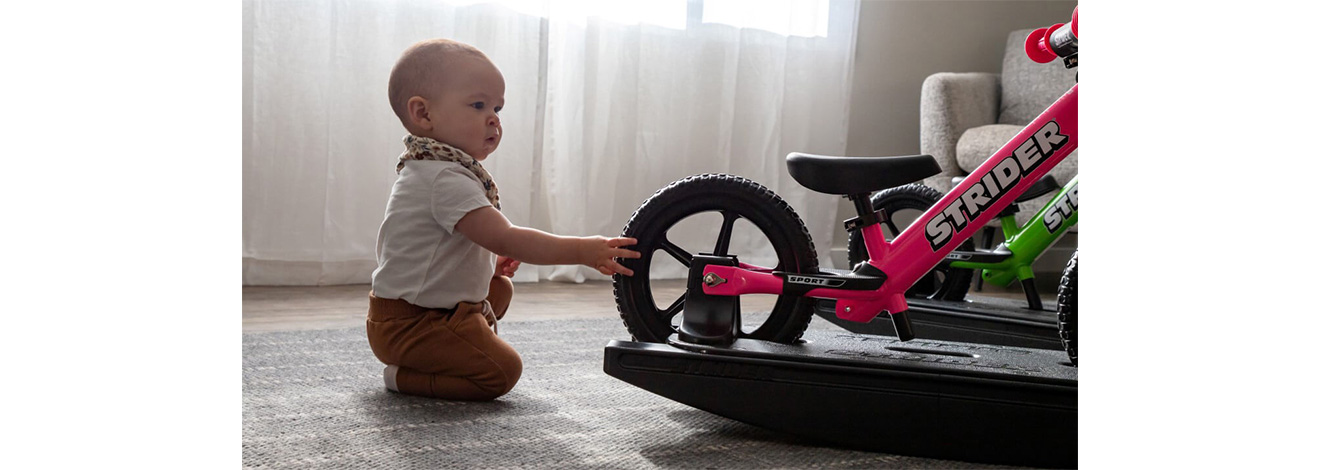 A baby checking out a pink Rocking Bike