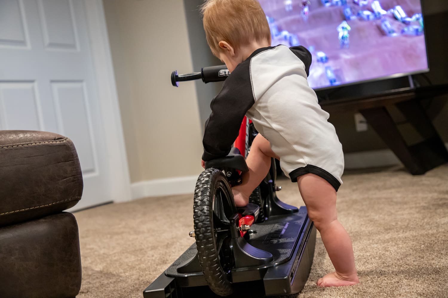 A toddler steps onto a red Strider Sport Rocking Bike
